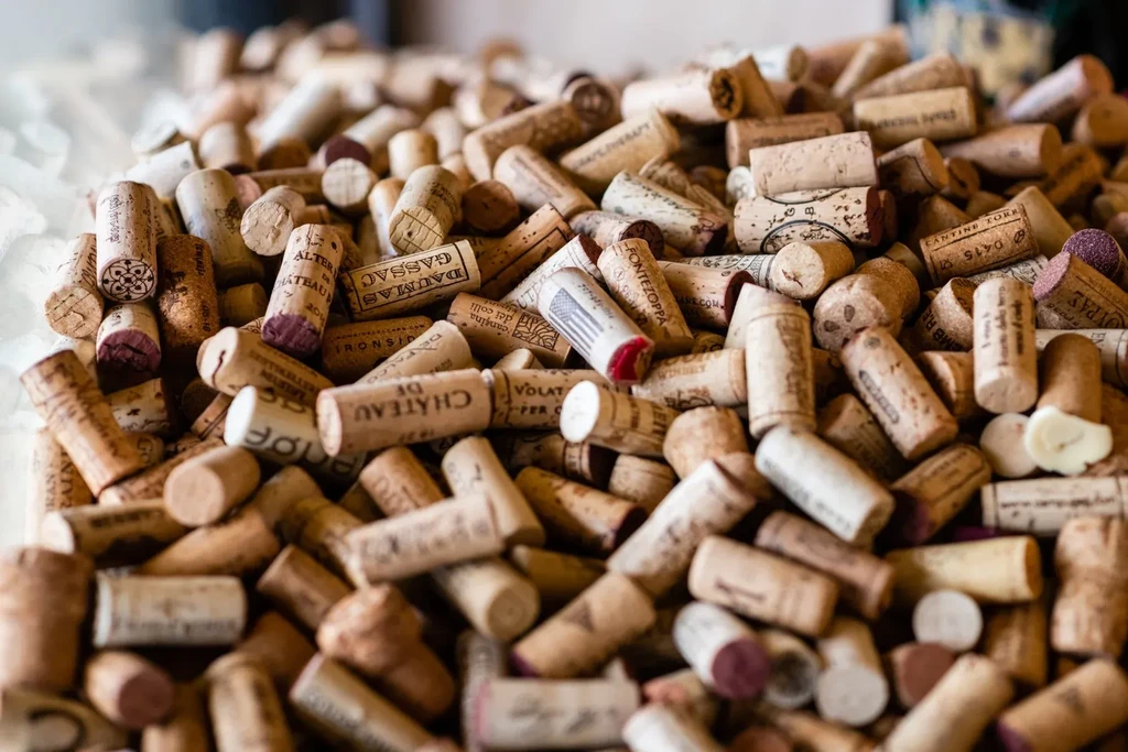 Dense pile of used wine corks with winery names and red stains.