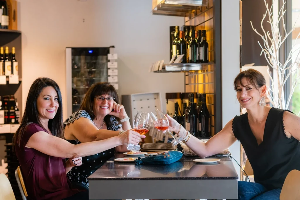 Three smiling women toast with rosé wine in a wine bar.