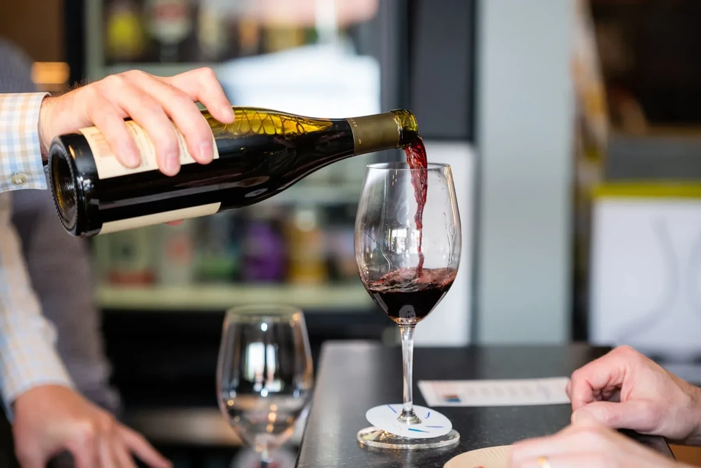Red wine pours from a dark bottle into a clear stemmed glass.