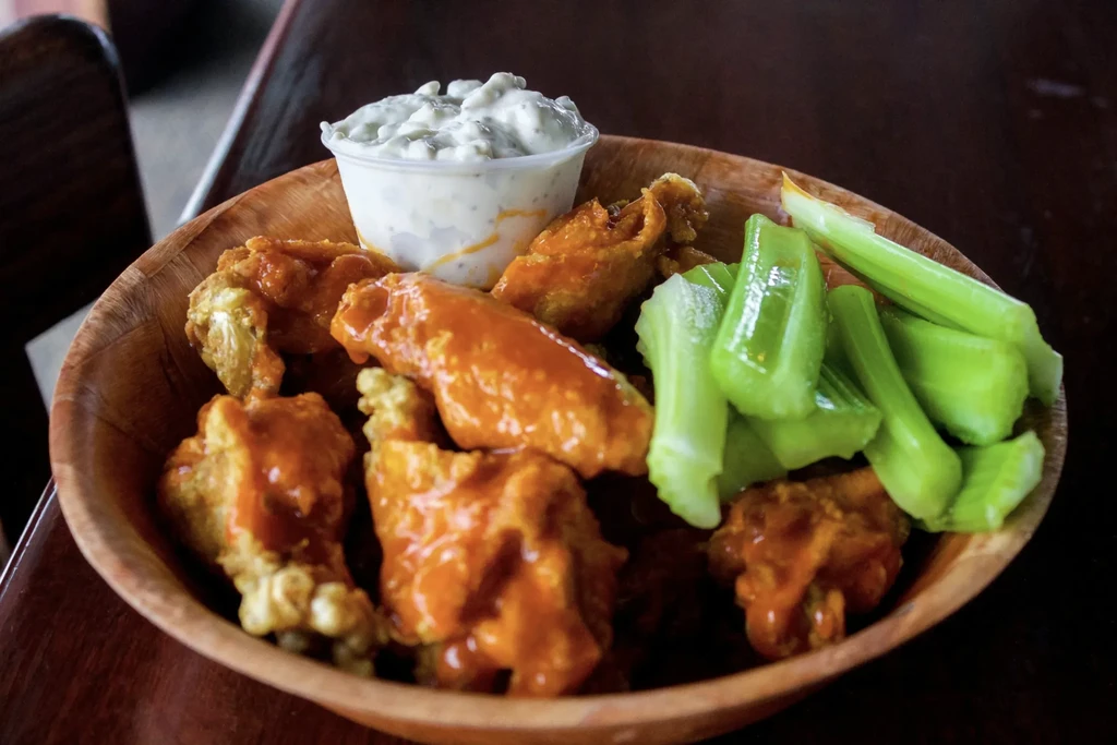 Wooden bowl with buffalo wings, celery sticks, and creamy dipping sauce.