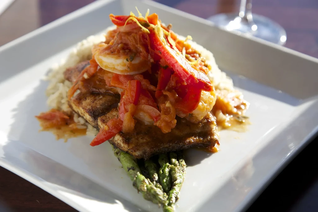 Close-up of fish, shrimp, rice, and vegetables with a red sauce.