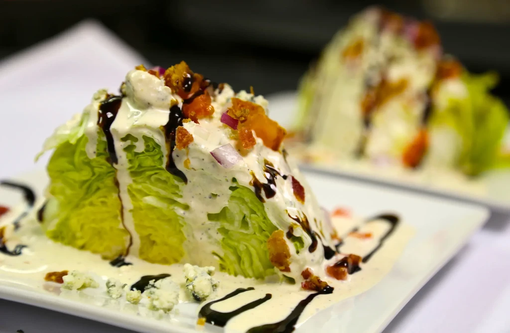 Two wedge salads with blue cheese, bacon, red onion, balsamic glaze.