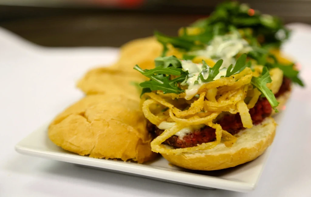 Two open-faced baguette sandwiches with patties, fried onions, and arugula.