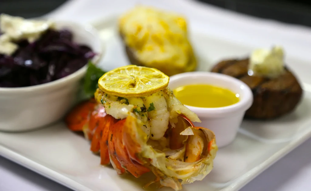 Prepared lobster tail with melted butter, steak, baked potato, and purple side.