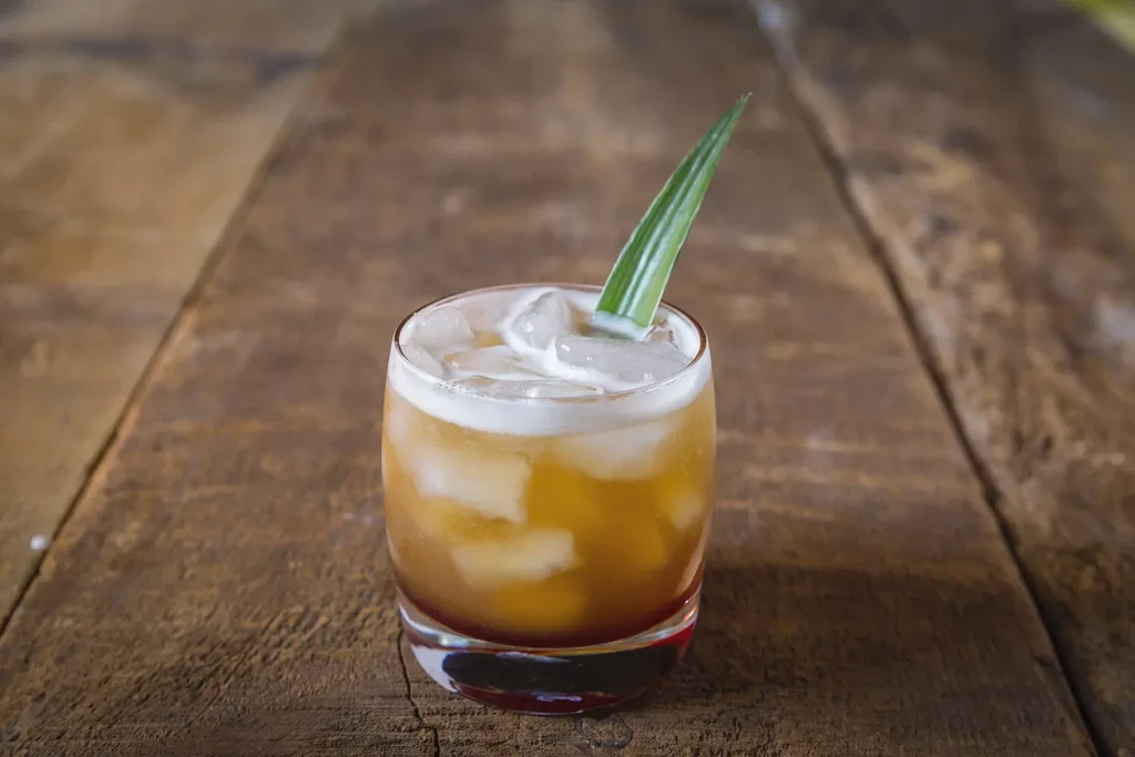 Layered cocktail with ice and green leaf garnish on a wooden table.