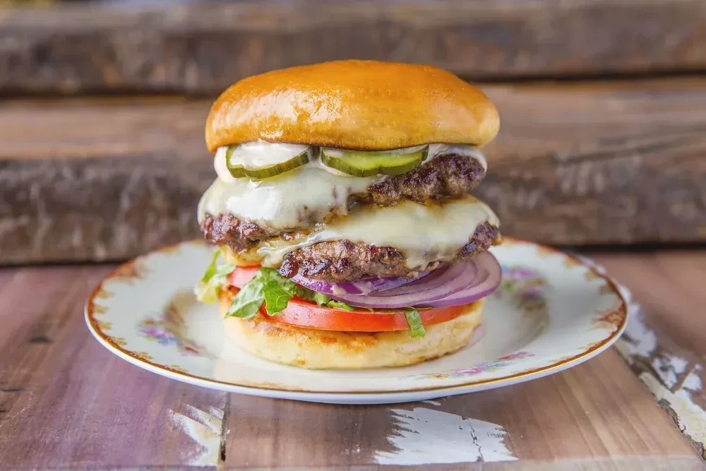 Well-stacked double cheeseburger on a floral plate and wooden table.