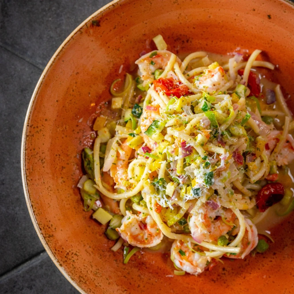Shrimp pasta with tomatoes, green vegetables, cheese, and herbs.