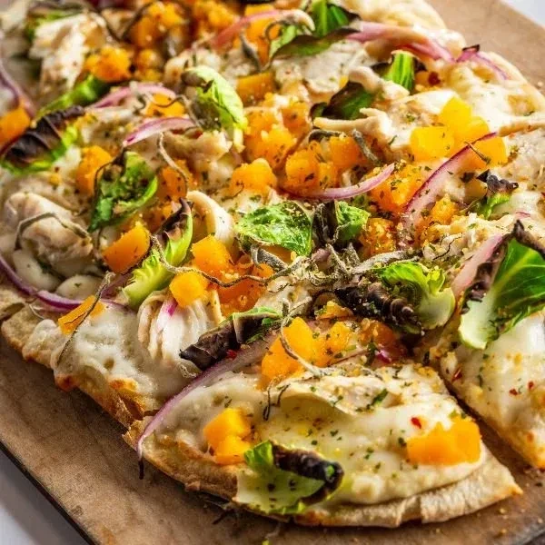 Rectangular flatbread with cheese, roasted squash, red onion, chicken, and greens.