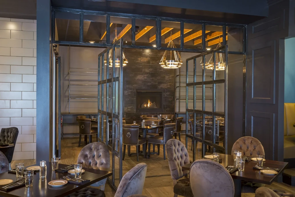 Restaurant interior with set tables, burning fireplace, glass dividers, and modern lighting.