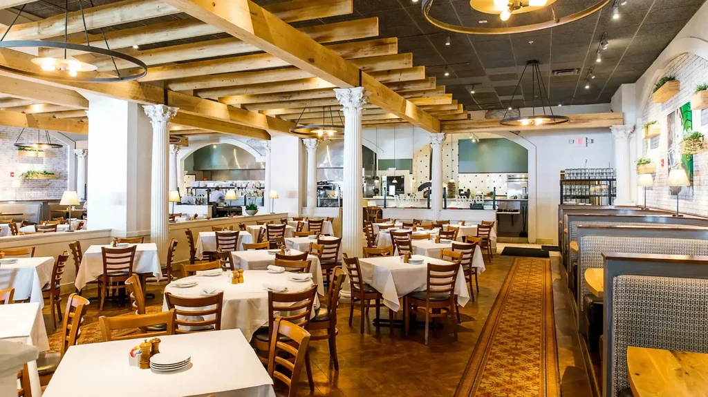 Spacious restaurant interior with wooden tables, upholstered booths, pillars, and exposed beams.