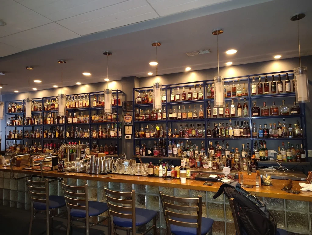 Well-lit empty bar with extensive whiskey bottle collection and stools.