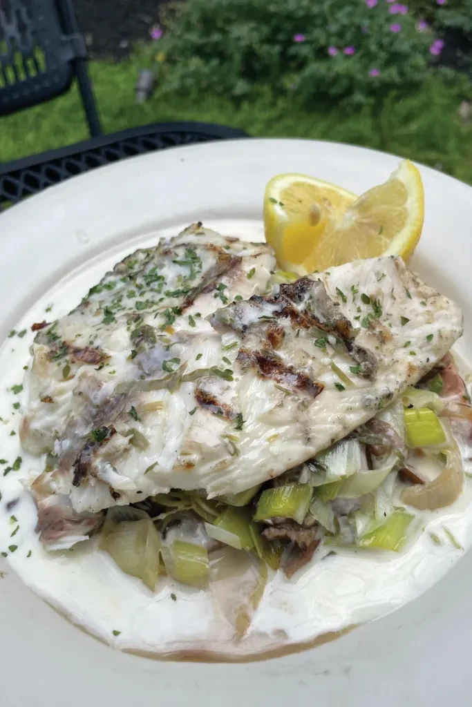 White fish fillet with leeks, creamy sauce, and lemon on a plate.