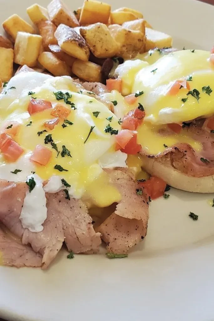 Eggs Benedict with hollandaise sauce, diced tomatoes, parsley, and potatoes.