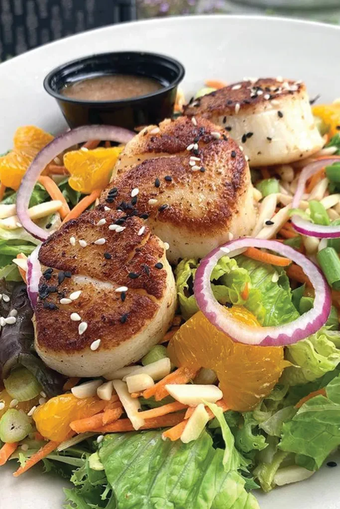 Three seared scallops with sesame seeds over a vibrant mixed green salad.
