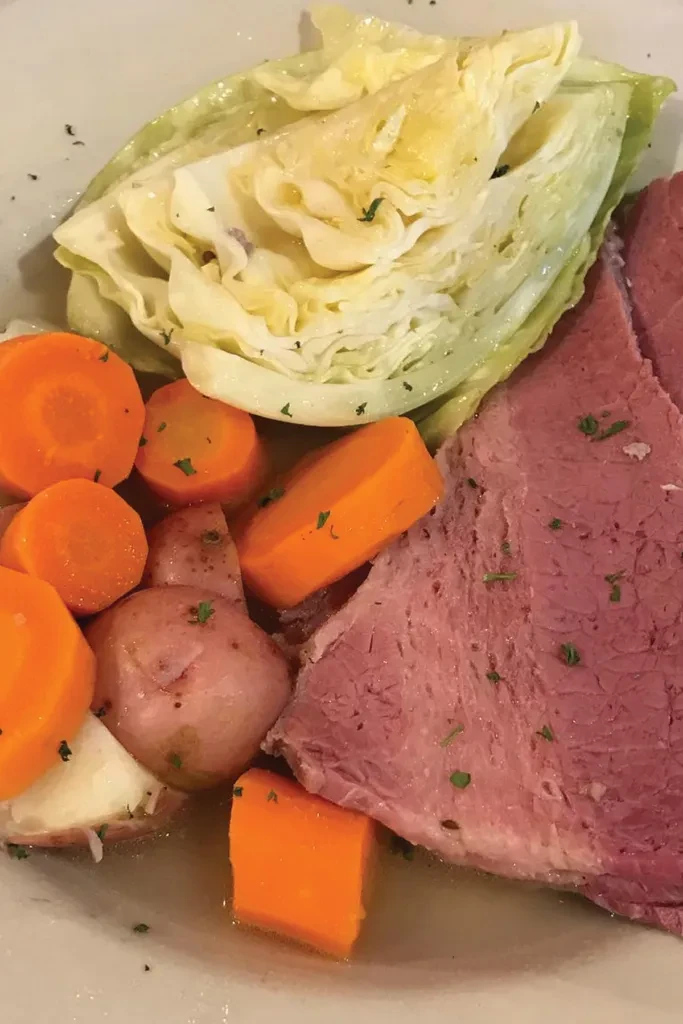 Cooked corned beef, cabbage, carrots, and potatoes on a white plate.