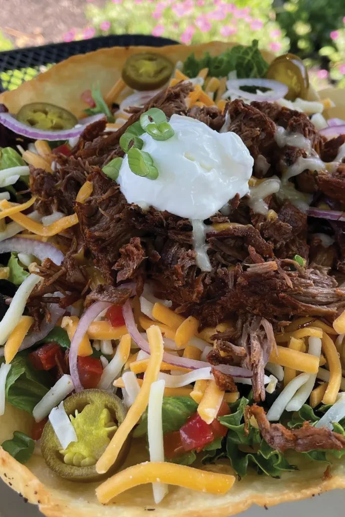 Taco salad in crispy tortilla bowl, topped with meat, cheese, and sour cream.