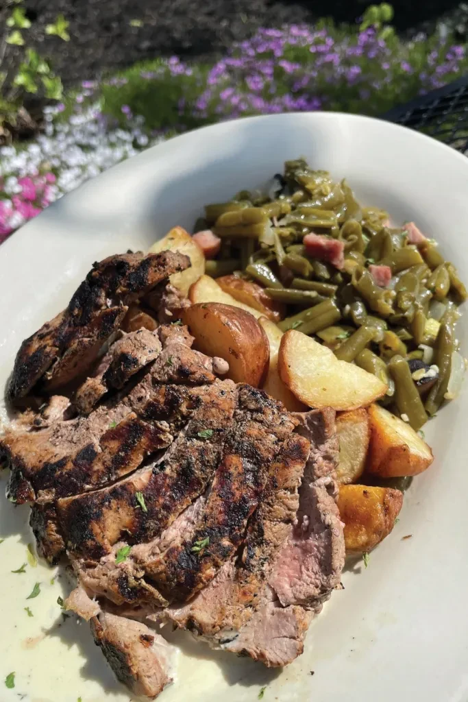 Plate of grilled meat, potato wedges, and green beans outdoors.