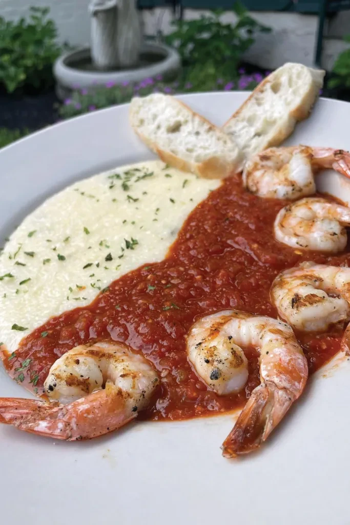 Plated shrimp and grits with tomato sauce, herbs, bread, outdoors.