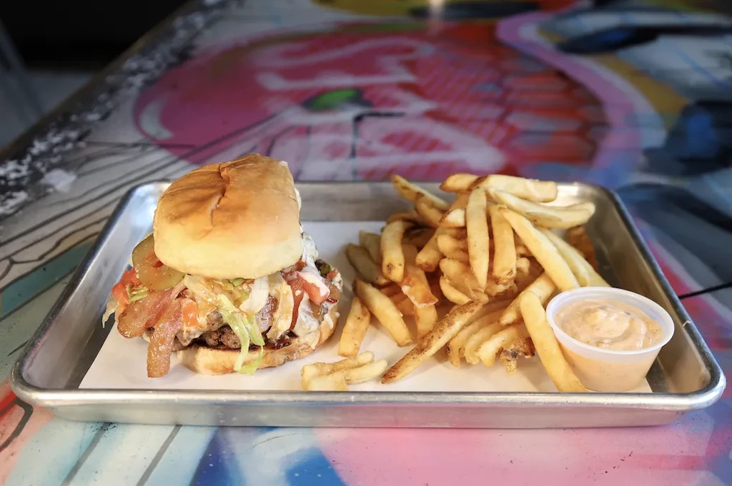 Gourmet burger, golden fries, and dipping sauce on a colorful table.