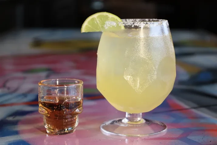 Margarita with lime, skull shot glass on a colorful surface.