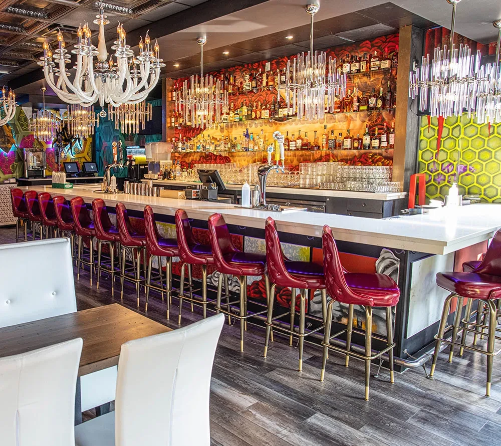 Empty bar, red stools, illuminated liquor display, skull-patterned wall.