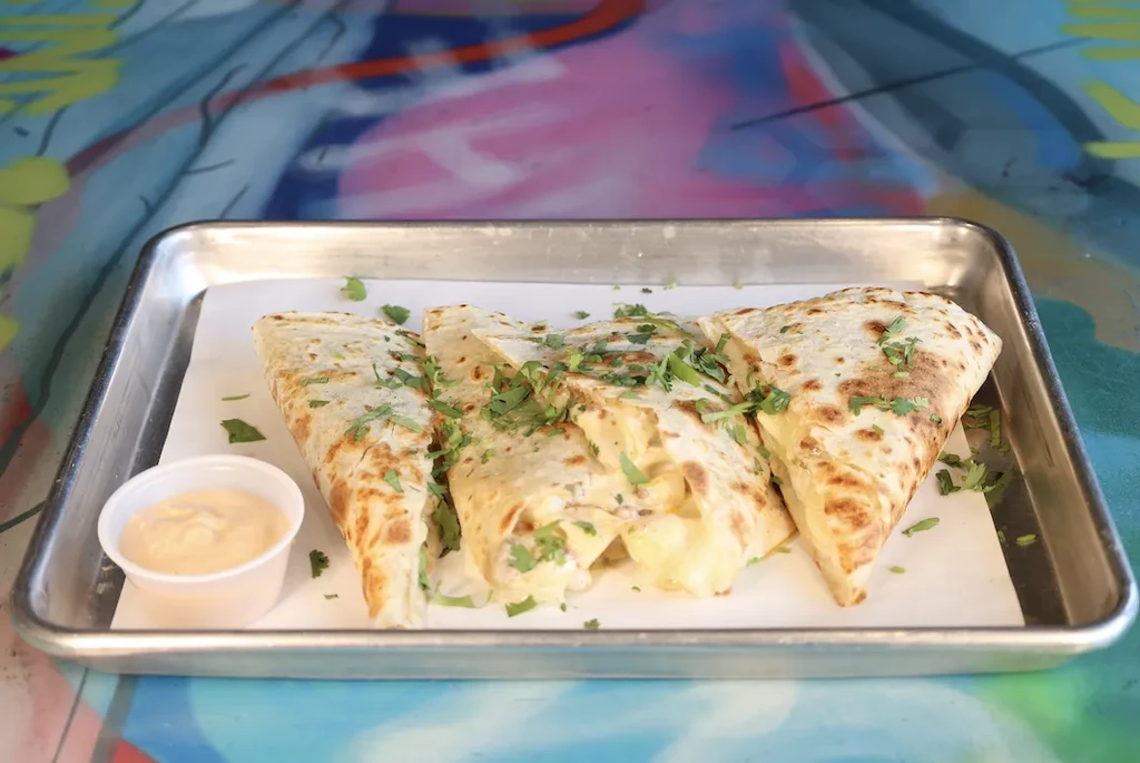 Quesadilla pieces with green herbs and sauce on a metal tray.