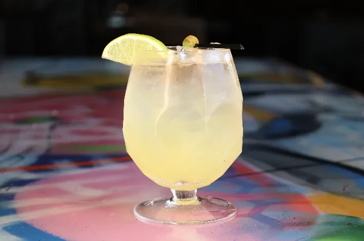 Cold pale yellow drink with lime wedge on colorful abstract surface.