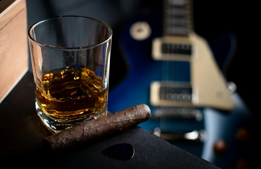 Rocks glass, cigar, guitar pick, and blurred blue electric guitar.