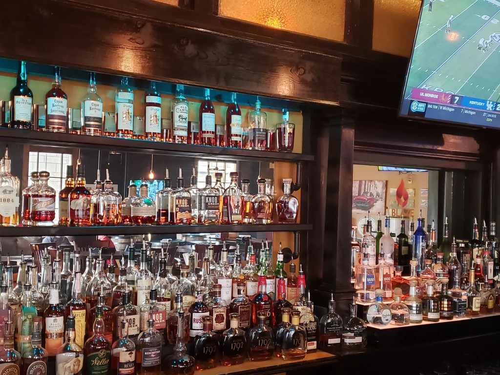Bar shelves packed with whiskey and bourbon, a TV shows football.