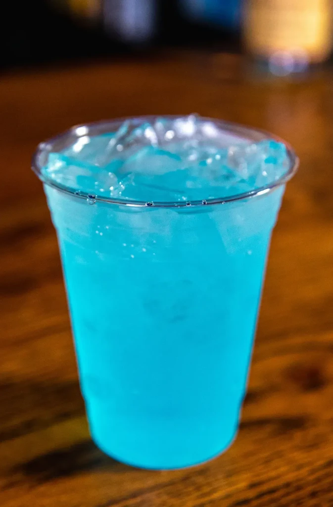 Electric blue iced drink in plastic cup on wood surface.