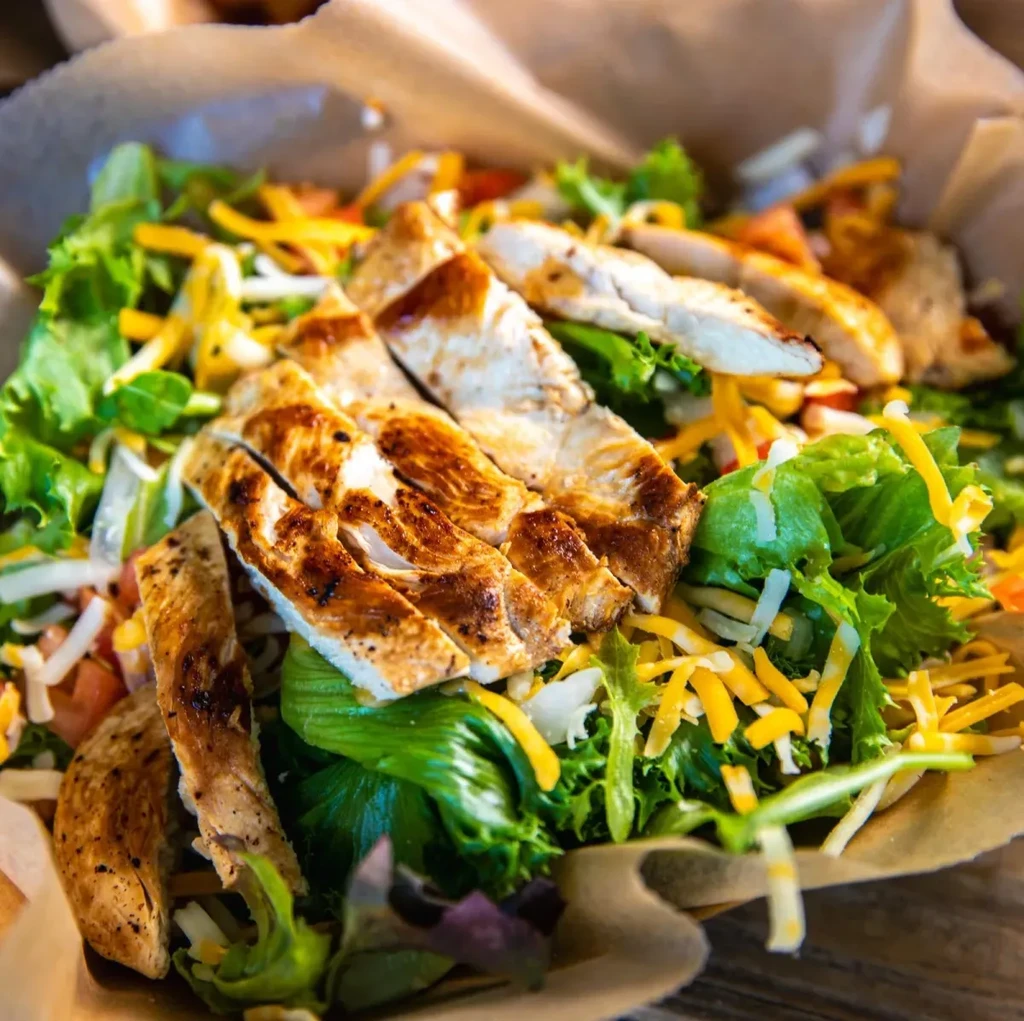 Fresh grilled chicken salad with cheese, tomatoes, and greens in a bowl.