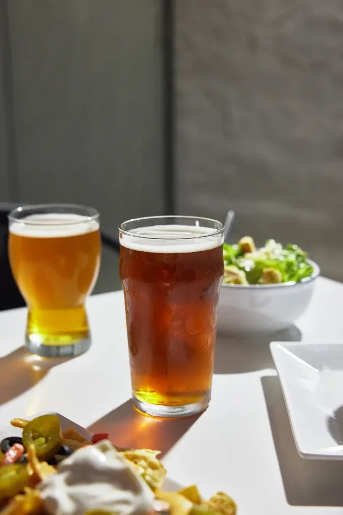 Two glasses of beer, nachos, and a salad on a table.