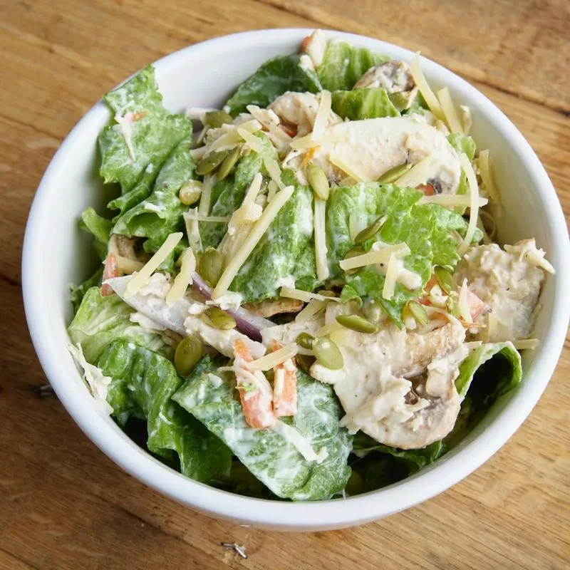 Mixed green salad with chicken, cheese, pepitas, and mushrooms on wood.
