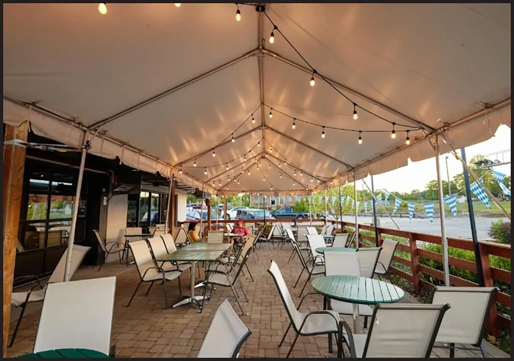 Well-lit outdoor patio under white tent with string lights and tables.