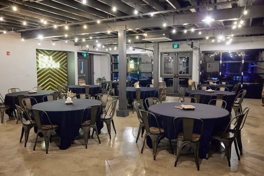 Industrial-chic event space: dark tables, fairy lights, 'THE MILL ROOM' sign.