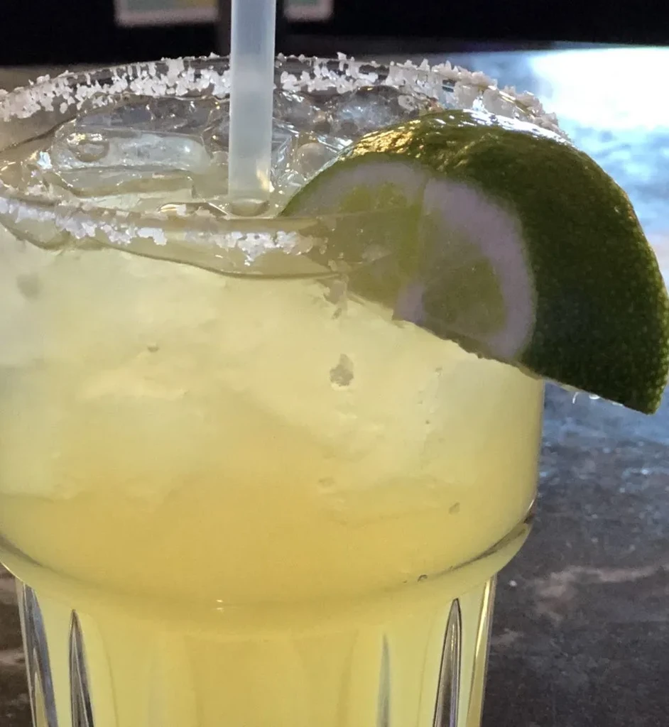 Close-up of a pale green drink with ice, salted rim, and lime.