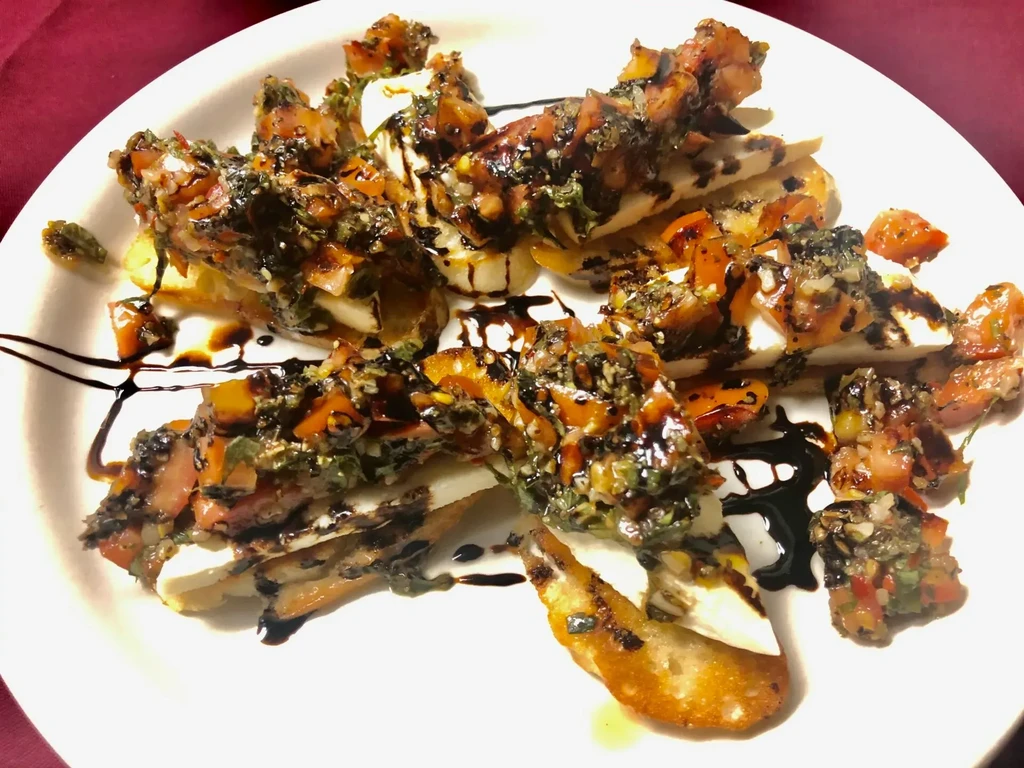 Bruschetta on a white plate with tomatoes, herbs, and balsamic glaze.