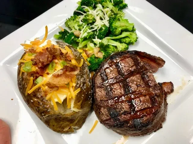 Grilled steak, loaded baked potato, and cheesy broccoli on a plate.