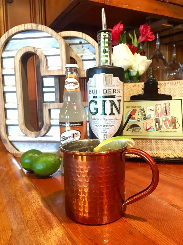 Lime-garnished drink in a hammered copper mug on a rustic bar.