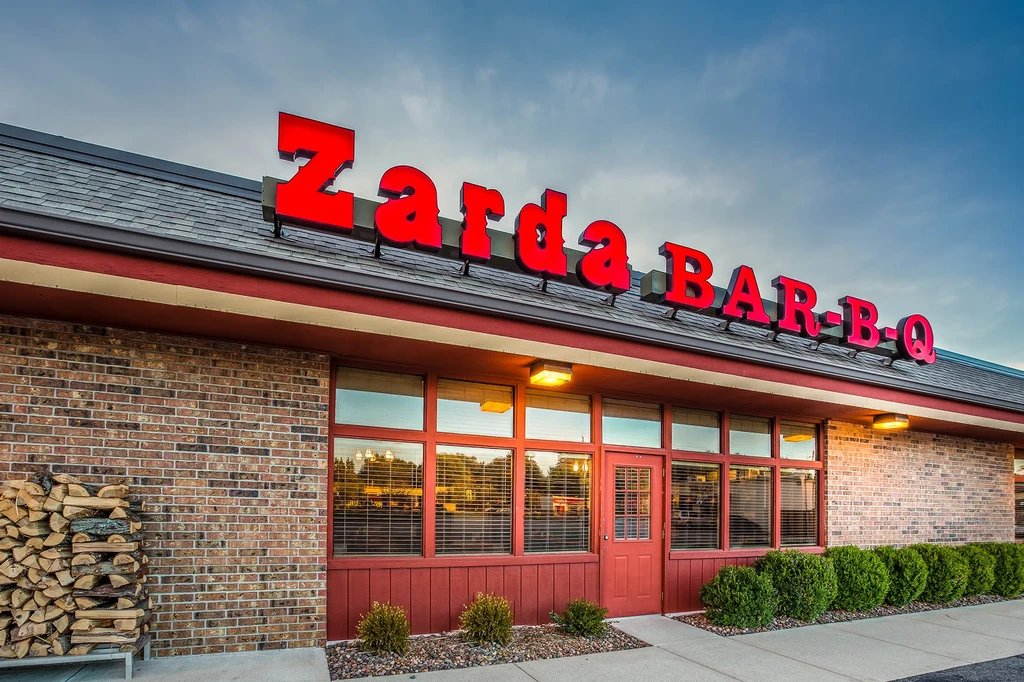 Exterior of Zarda BAR-B-Q restaurant with prominent sign and firewood.