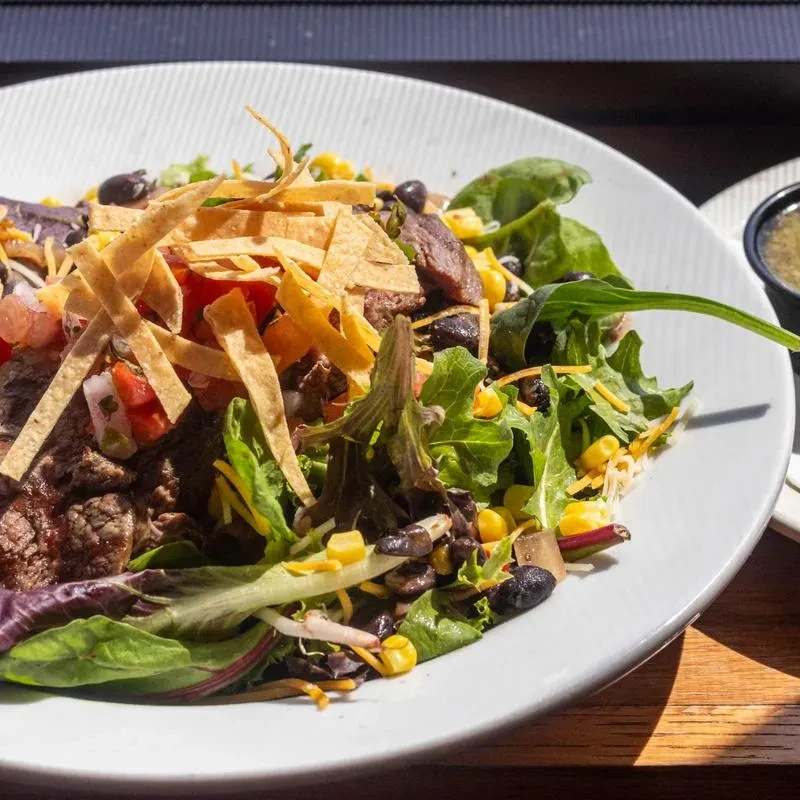 Colorful salad with meat, beans, corn, cheese, pico de gallo, and tortilla strips.
