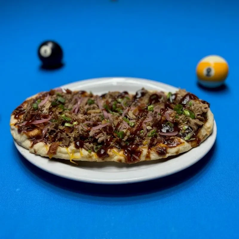 Savory flatbread with BBQ meat, onions, and cheese on a pool table.