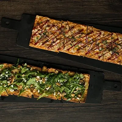 Two rectangular flatbreads: one savory with sauce, one with arugula and cheese.