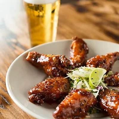 Dark-glazed chicken wings with sesame seeds, cabbage slaw, and a beer.