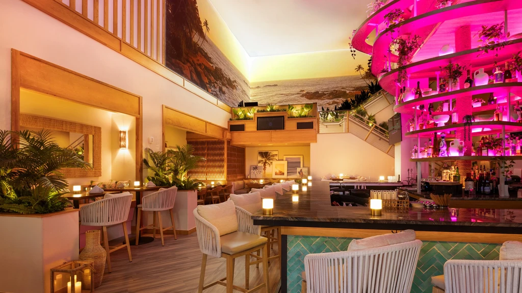 Modern restaurant bar with pink-lit shelves and a tropical mural.