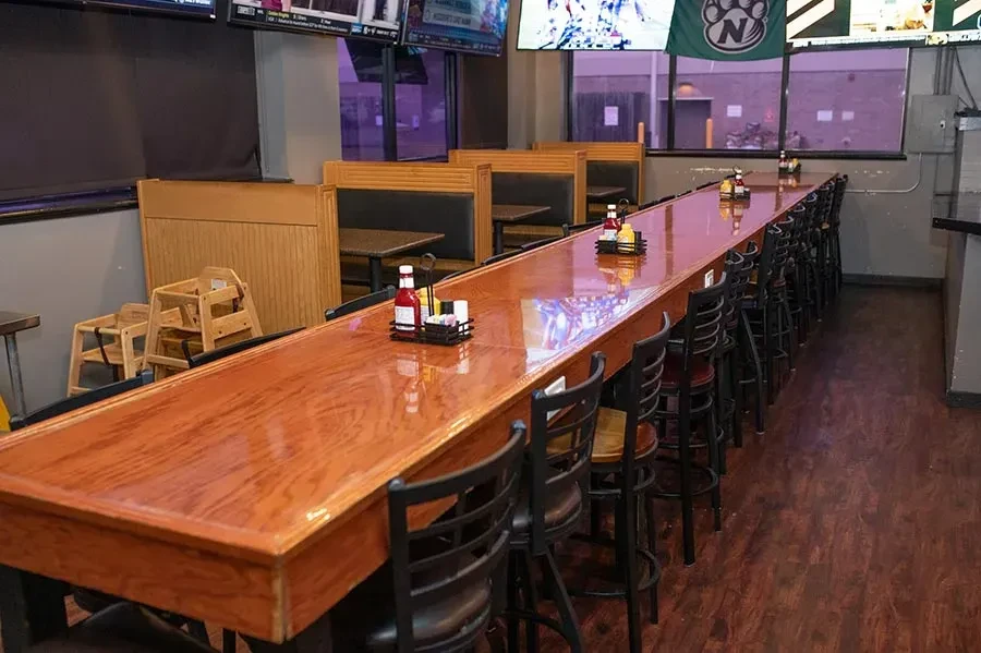 Empty casual sports bar interior with a long wooden bar and TVs.
