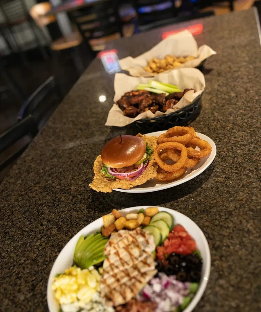 Variety of prepared restaurant dishes: salad, sandwich, wings, appetizers.