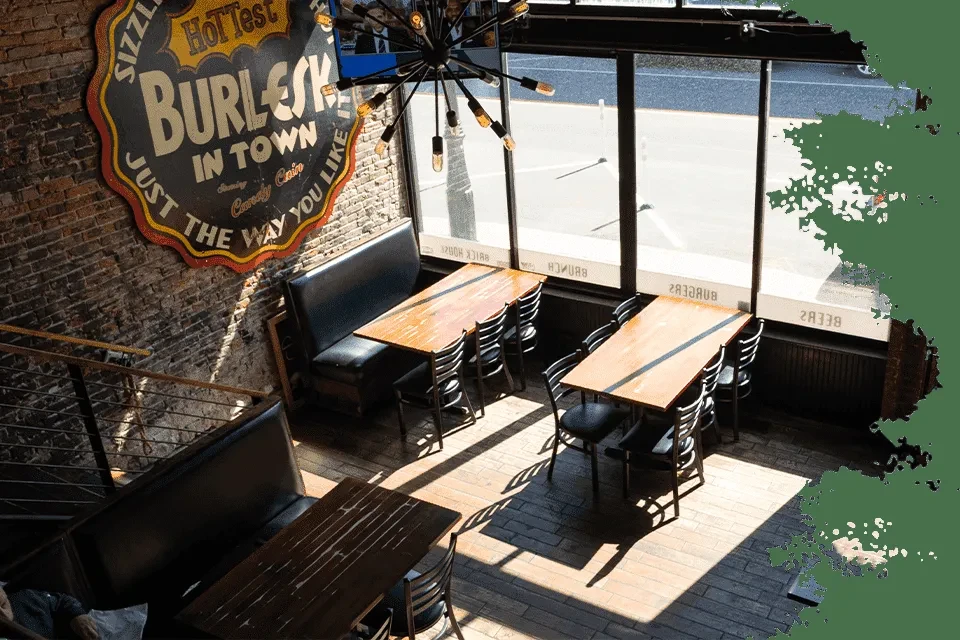 Industrial-rustic restaurant interior with vintage burlesque sign and sunlight.