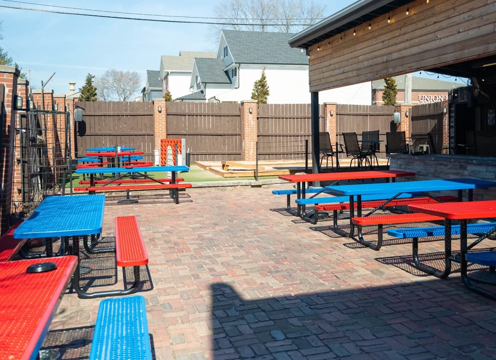 Outdoor restaurant patio with red and blue picnic and high-top tables.