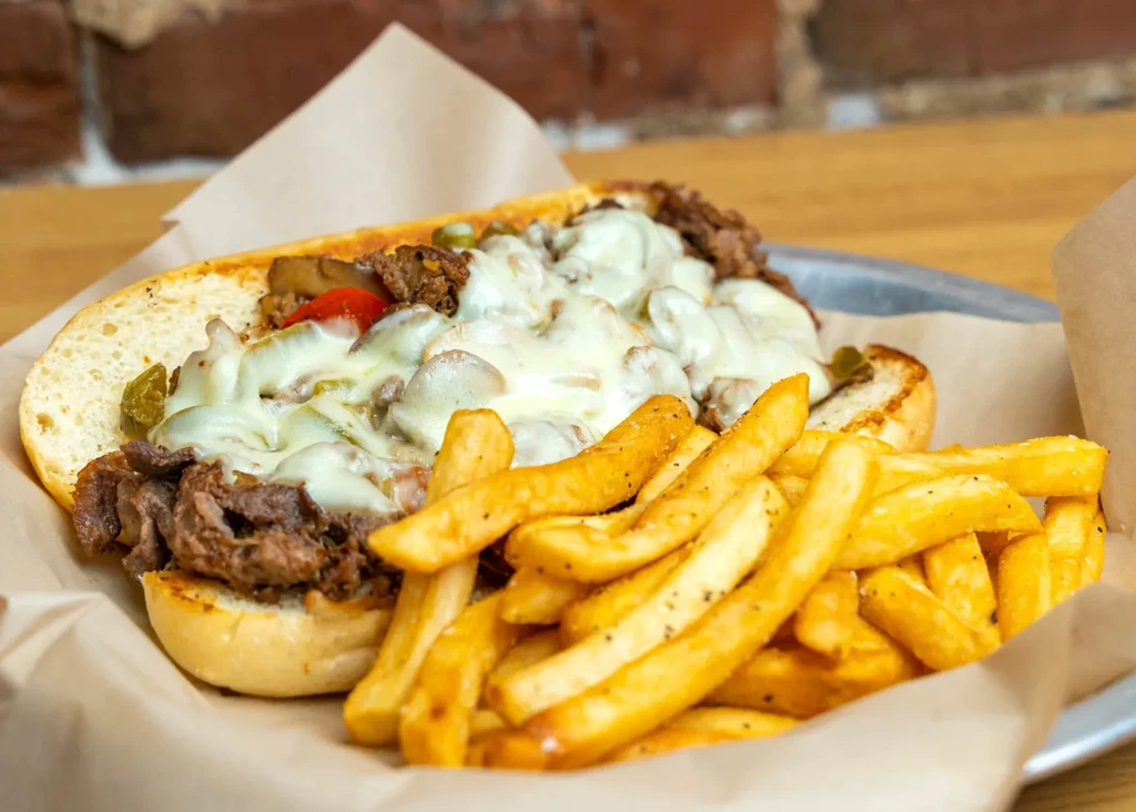 Grilled cheesesteak sandwich with melted cheese, vegetables, and golden french fries.